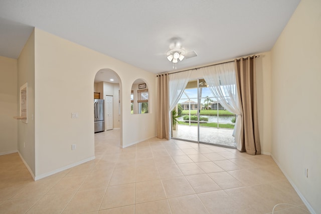 empty room with arched walkways, light tile patterned flooring, ceiling fan, and baseboards