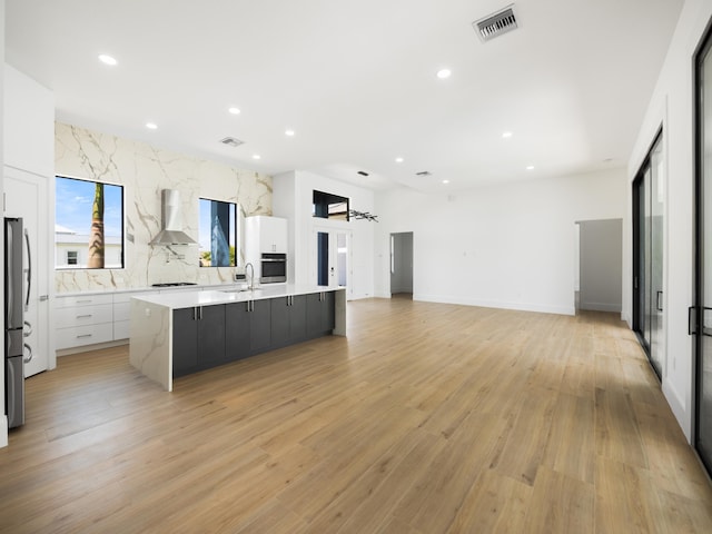 kitchen with a spacious island, white cabinetry, light hardwood / wood-style floors, and wall chimney exhaust hood