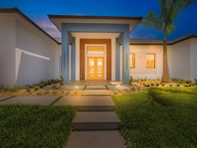 exterior entry at dusk featuring french doors and a lawn