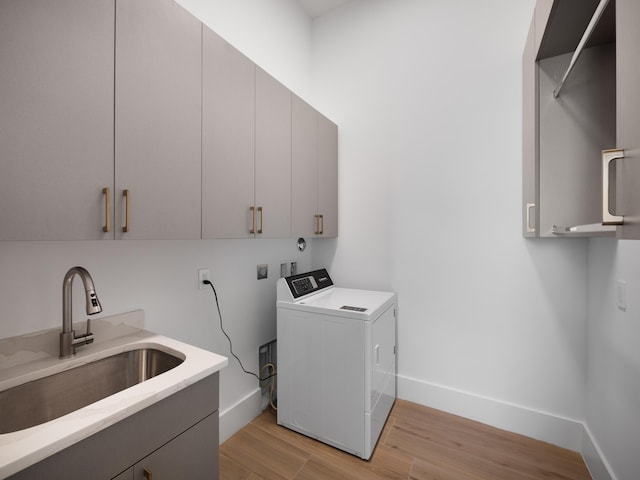 clothes washing area featuring washer / dryer, light hardwood / wood-style flooring, sink, and cabinets