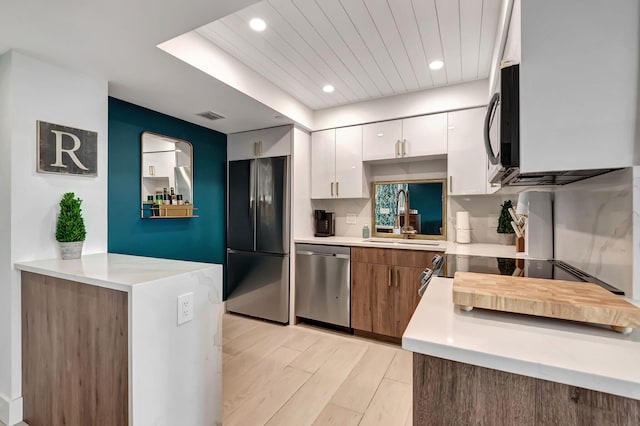 kitchen featuring sink, light wood-type flooring, kitchen peninsula, stainless steel appliances, and white cabinets