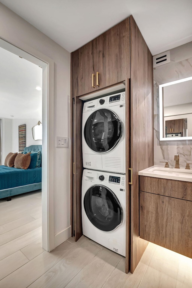 washroom with sink, light hardwood / wood-style floors, and stacked washing maching and dryer