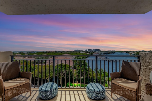 balcony at dusk featuring a water view