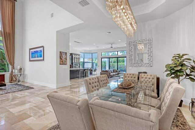 dining space with baseboards, ceiling fan with notable chandelier, a towering ceiling, and visible vents