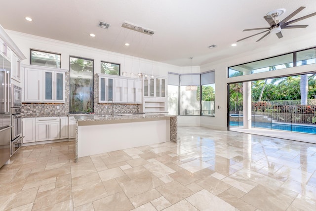 kitchen with white cabinetry, light stone counters, tasteful backsplash, and an island with sink