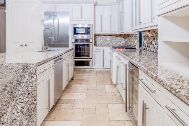 kitchen featuring white cabinetry, light stone countertops, built in appliances, and beverage cooler