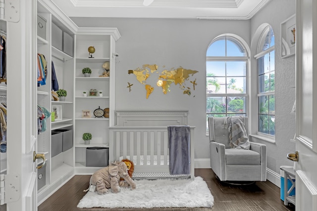 bedroom with a nursery area, ornamental molding, and dark hardwood / wood-style flooring