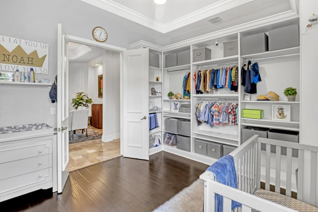 bedroom featuring a raised ceiling, ornamental molding, dark hardwood / wood-style floors, and a nursery area