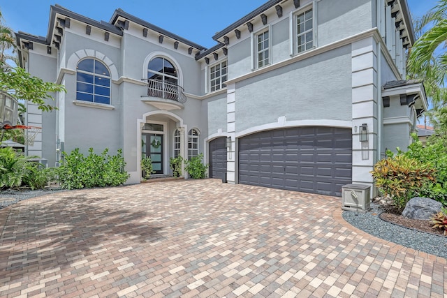 view of front of property with an attached garage, stucco siding, decorative driveway, and a balcony