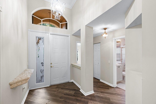 entrance foyer featuring an inviting chandelier, ornamental molding, and dark wood-type flooring