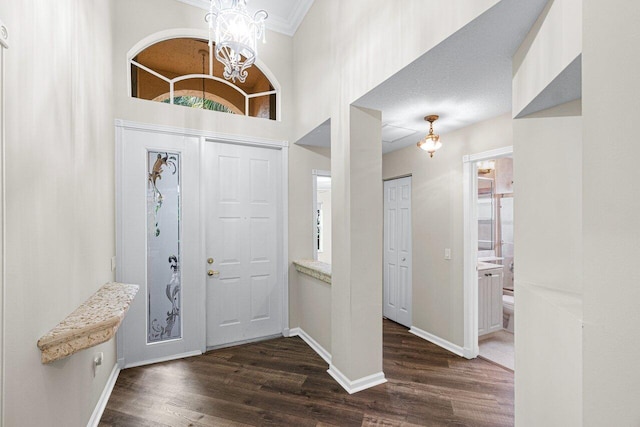 entryway featuring an inviting chandelier, crown molding, baseboards, a towering ceiling, and dark wood finished floors