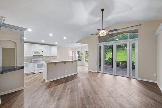 kitchen with wood finished floors, white appliances, a kitchen bar, baseboards, and a ceiling fan