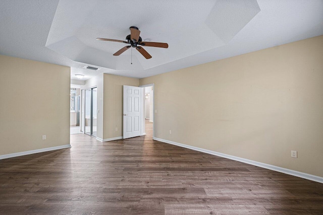 unfurnished room with dark wood-style floors, ceiling fan, a raised ceiling, and baseboards