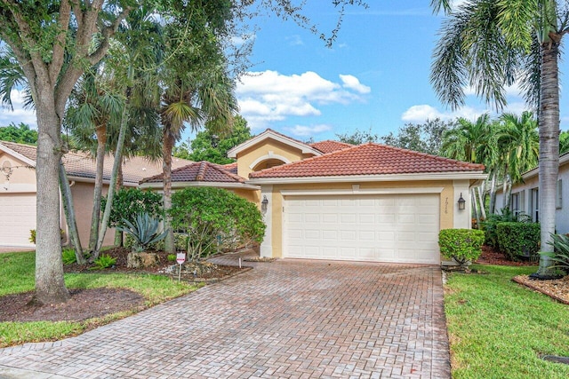 mediterranean / spanish-style home with decorative driveway, an attached garage, a tiled roof, and stucco siding