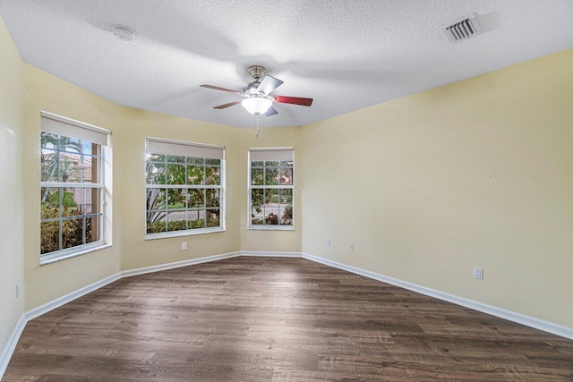 spare room with a textured ceiling, visible vents, baseboards, dark wood-style flooring, and a ceiling fan