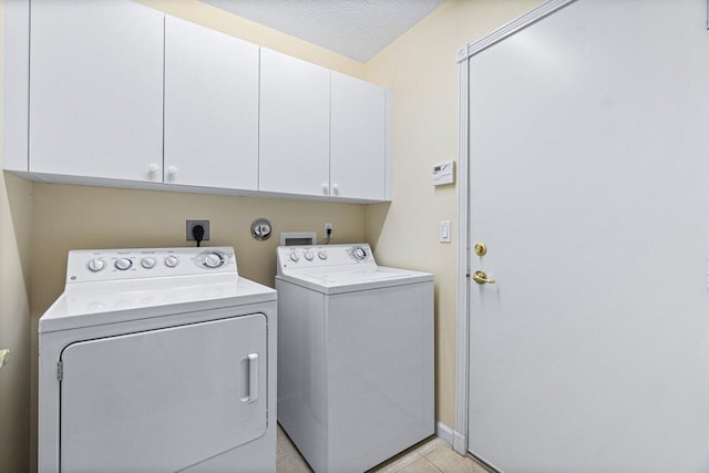 clothes washing area with light tile patterned floors, a textured ceiling, cabinets, and separate washer and dryer