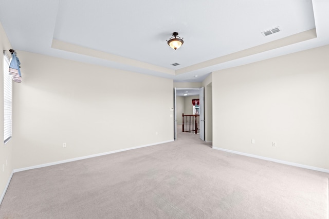 empty room with a raised ceiling and light carpet