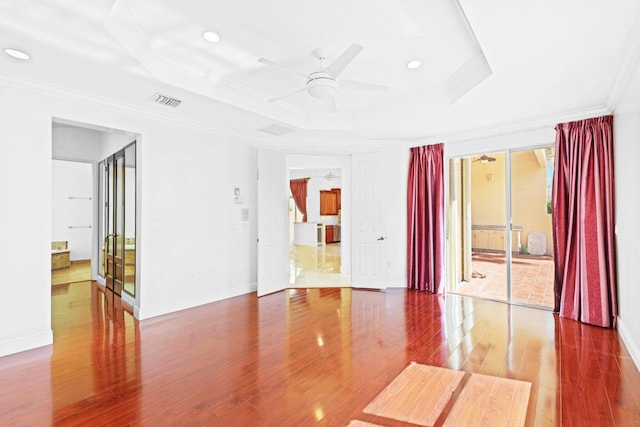 spare room featuring wood-type flooring, a tray ceiling, ceiling fan, and crown molding