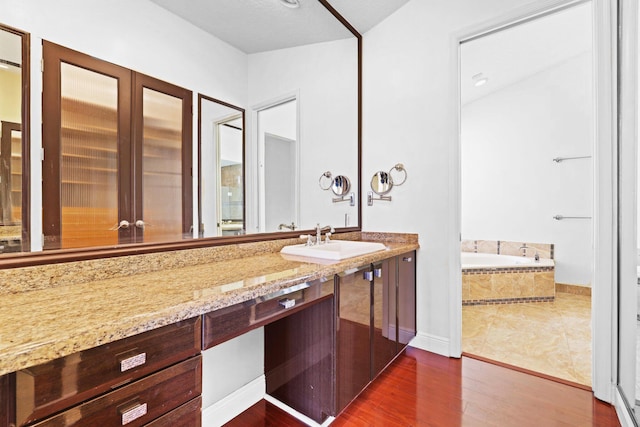 bathroom featuring vanity, wood-type flooring, and tiled tub