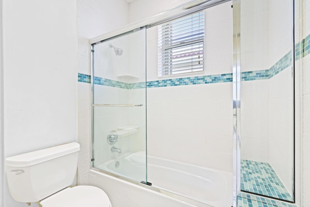 bathroom featuring toilet and shower / bath combination with glass door