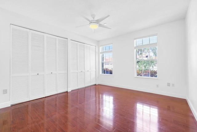 unfurnished bedroom featuring multiple closets, ceiling fan, and wood-type flooring