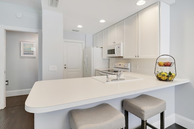 kitchen featuring white cabinets, a kitchen breakfast bar, white appliances, and kitchen peninsula