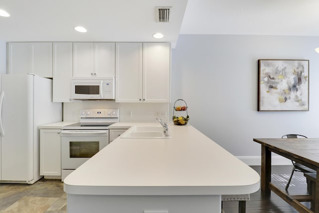 kitchen with white appliances, white cabinets, sink, a kitchen bar, and kitchen peninsula