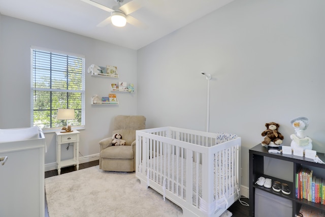 bedroom with ceiling fan, a nursery area, and wood-type flooring