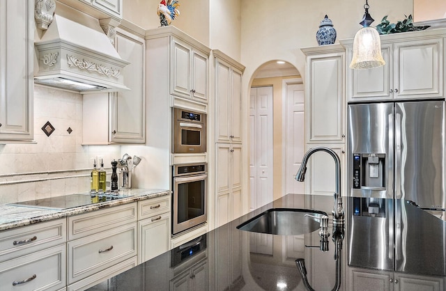 kitchen featuring light stone countertops, sink, stainless steel fridge, hanging light fixtures, and custom exhaust hood