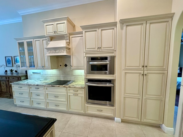 kitchen with decorative backsplash, cream cabinets, black stovetop, and light tile patterned floors