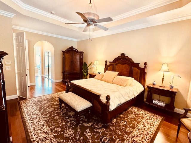 bedroom with crown molding, hardwood / wood-style flooring, a tray ceiling, and ceiling fan