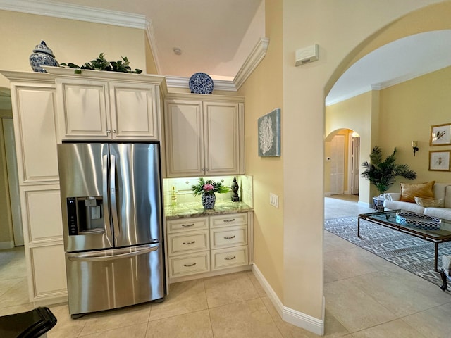 kitchen with ornamental molding, stainless steel fridge, light stone countertops, and cream cabinetry