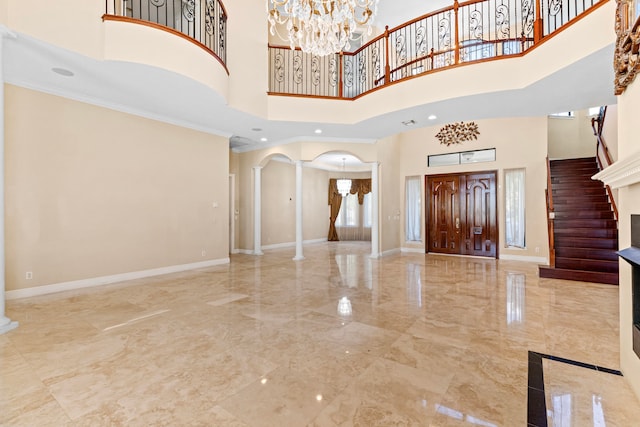 entryway featuring ornate columns, ornamental molding, a high ceiling, and an inviting chandelier