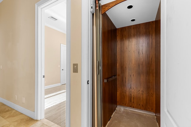 hall with crown molding, wood walls, and elevator