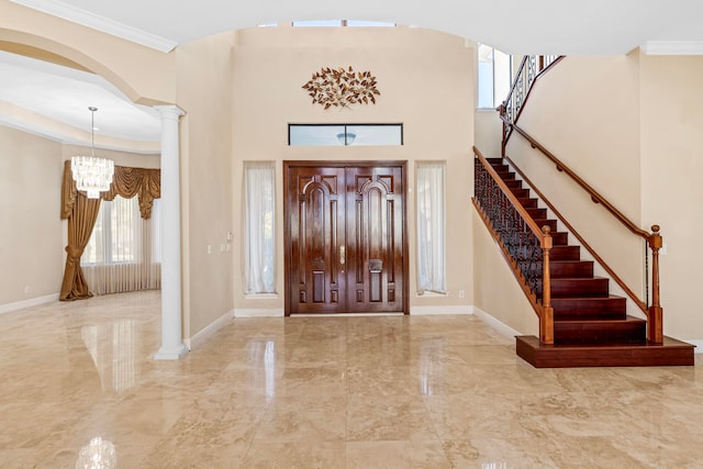 foyer entrance featuring ornamental molding, decorative columns, and a chandelier