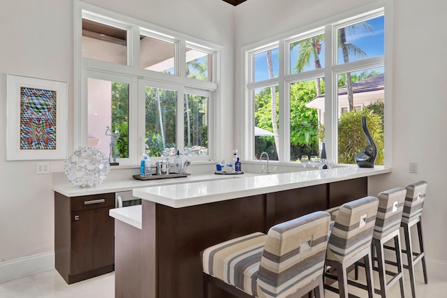 kitchen featuring dark brown cabinetry, light tile patterned floors, kitchen peninsula, and a kitchen bar