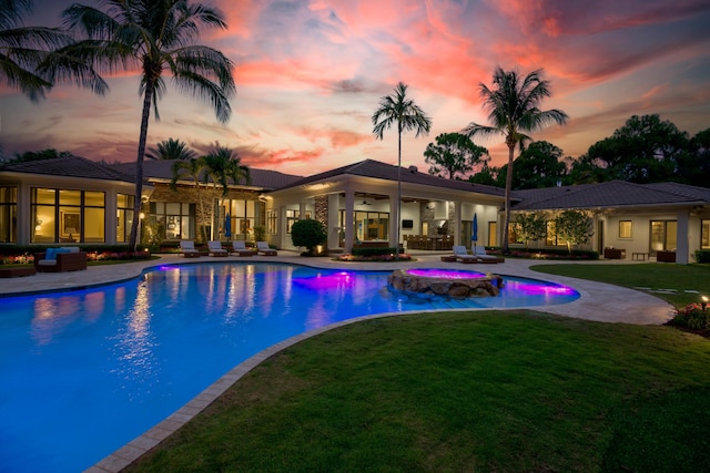 pool at dusk featuring an in ground hot tub, a patio, ceiling fan, and a lawn