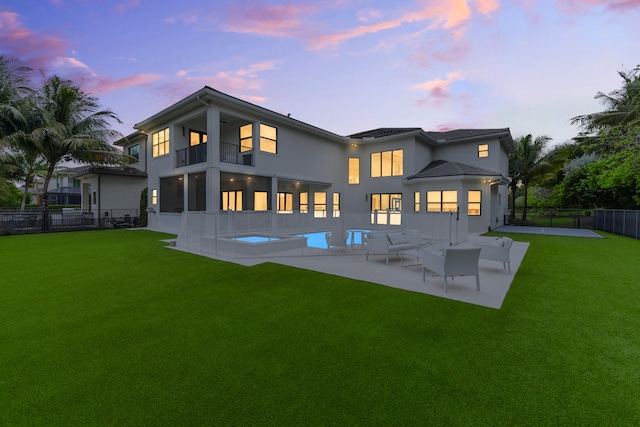 back house at dusk featuring a patio, a fenced in pool, a yard, and a balcony