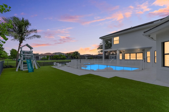 pool at dusk featuring a patio area, a lawn, and a playground