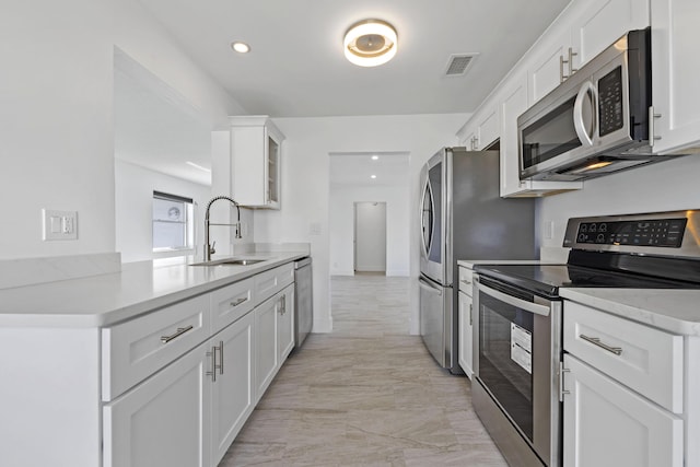 kitchen featuring kitchen peninsula, light stone counters, stainless steel appliances, sink, and white cabinetry