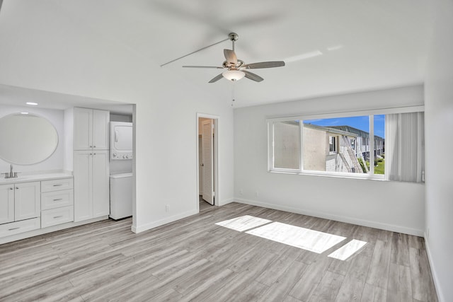 unfurnished bedroom featuring ceiling fan, light hardwood / wood-style flooring, ensuite bathroom, stacked washer and dryer, and sink