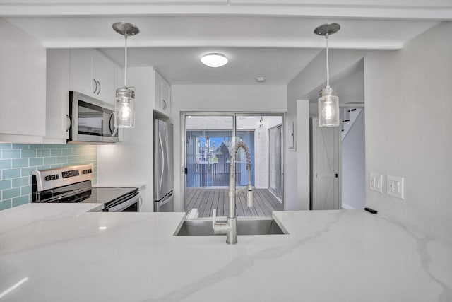 kitchen with white cabinets, hanging light fixtures, backsplash, appliances with stainless steel finishes, and sink