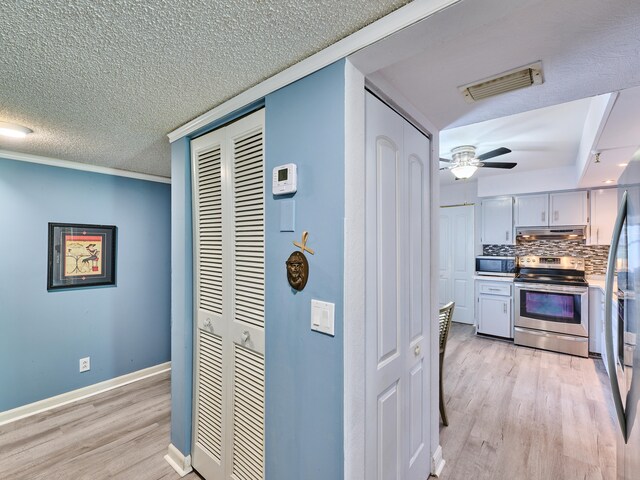 kitchen featuring light wood-type flooring, tasteful backsplash, ornamental molding, stainless steel appliances, and ceiling fan