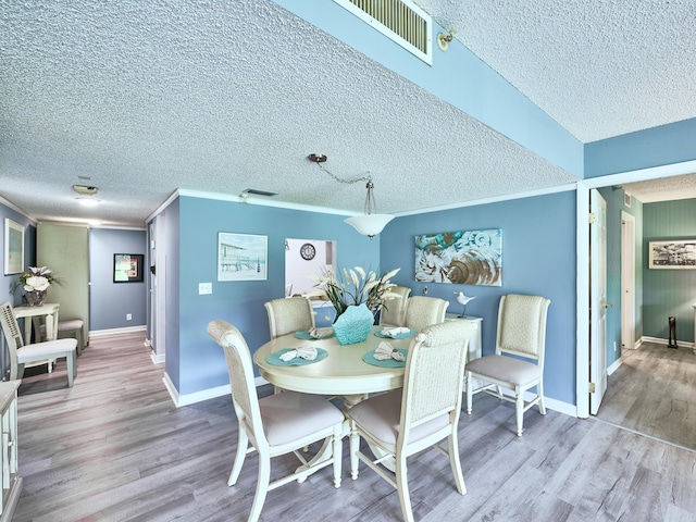 dining area with light hardwood / wood-style floors, ornamental molding, and a textured ceiling