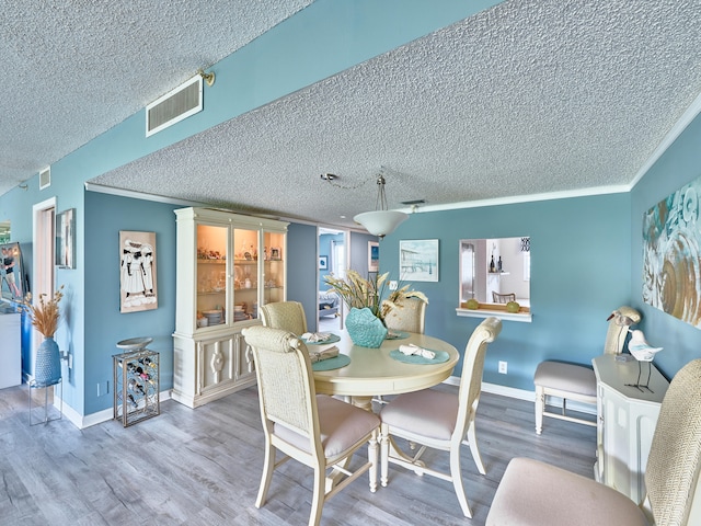 dining space featuring wood-type flooring, a textured ceiling, and ornamental molding