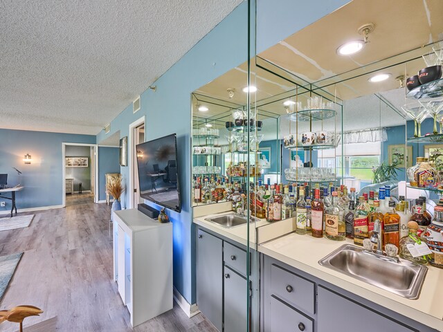 bar featuring a textured ceiling, light hardwood / wood-style flooring, and sink