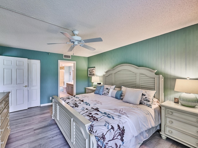 bedroom with ceiling fan, a textured ceiling, connected bathroom, and dark wood-type flooring