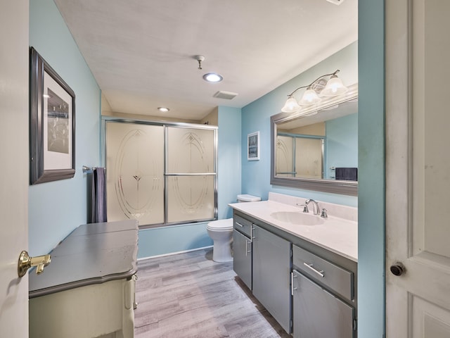 full bathroom with vanity, hardwood / wood-style flooring, toilet, and bath / shower combo with glass door