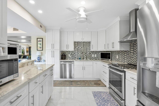 kitchen featuring wall chimney range hood, white cabinets, stainless steel appliances, and light stone counters