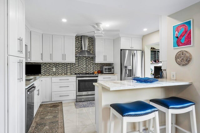 kitchen with light stone countertops, a kitchen bar, stainless steel appliances, wall chimney exhaust hood, and white cabinets